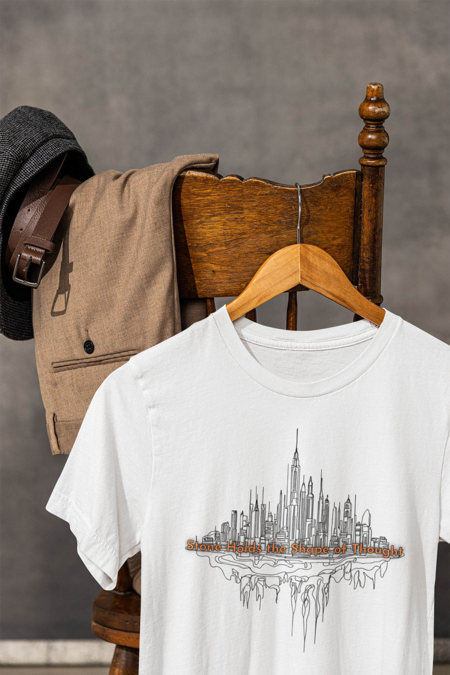 White t-shirt with architectural cityscape design by Studio Nature Design on a wooden chair against a gray background