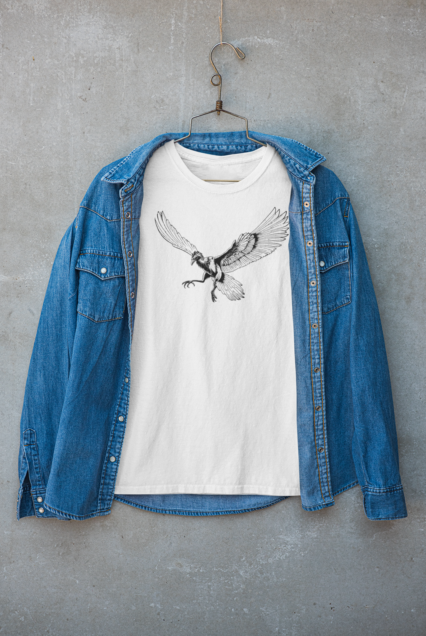 Unisex white T-shirt with black line art of Archaeopteryx fossil bird, minimalist prehistoric design for science and nature lovers and blue denim jacket on a gray surface
