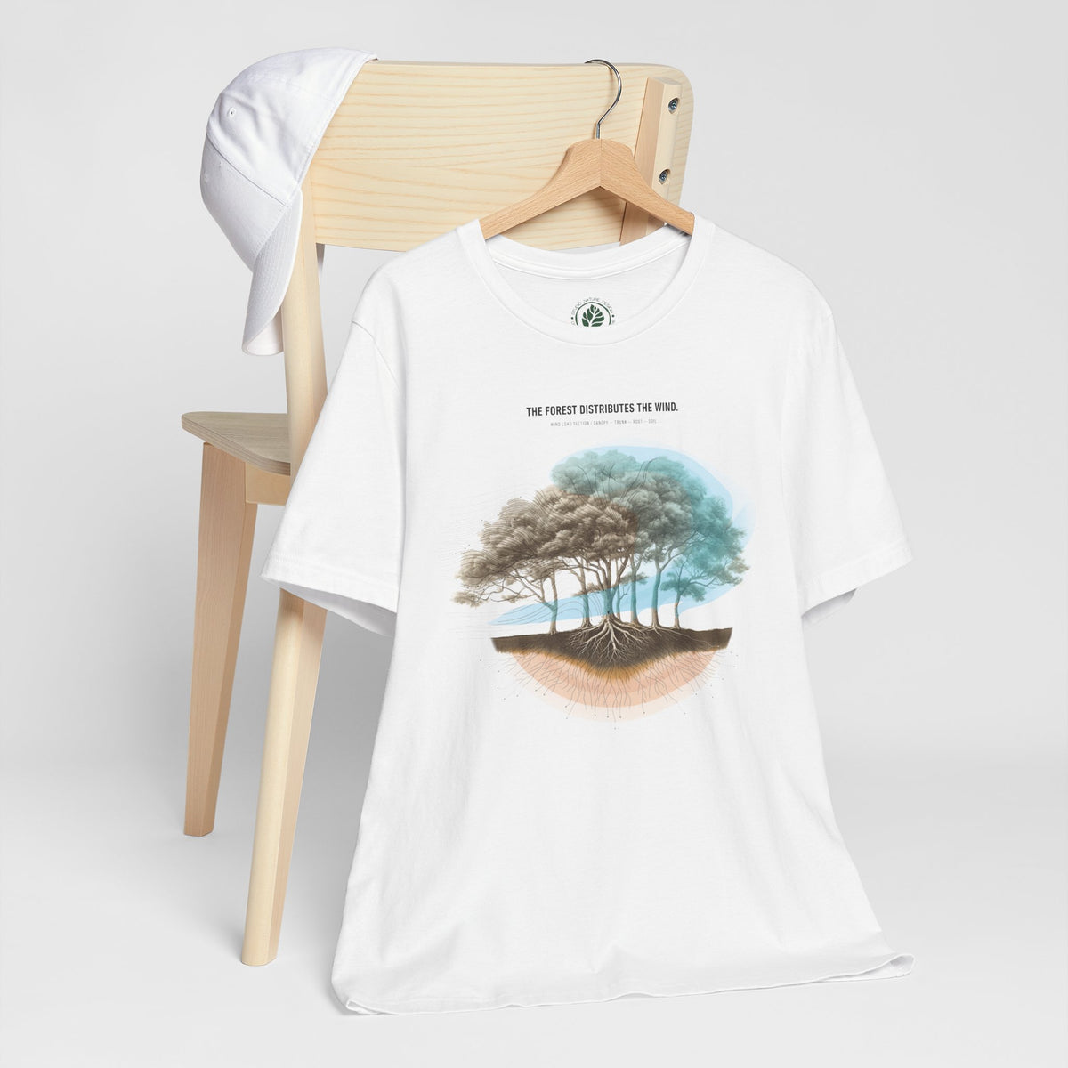 White Forest Under Wind Load T-shirt hanging beside neutral garments, showing the full front artwork.