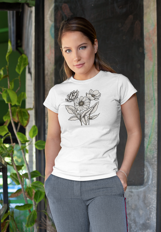 Woman wearing a white Monochrome Bloom Tee with a hand-drawn black floral design, standing near green potted plants in a sunlit urban space.
