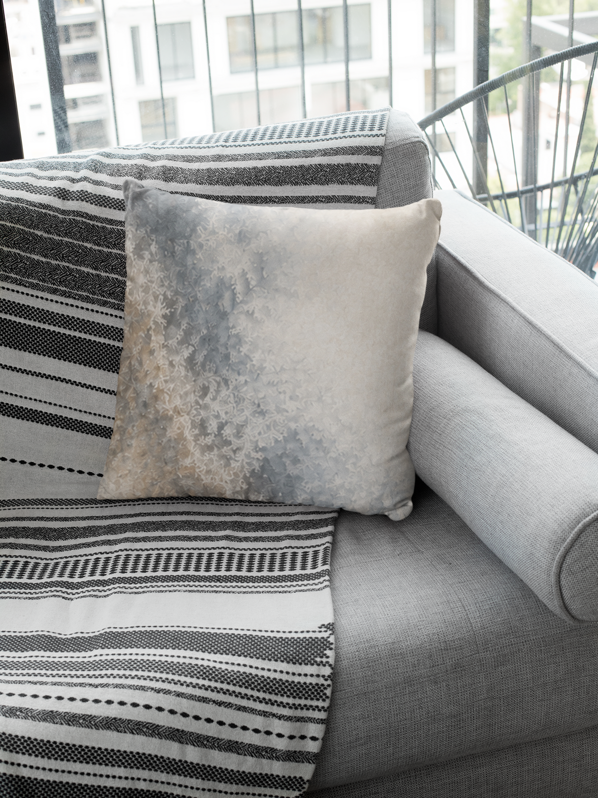 Frost Veil faux suede pillowcase on a grey fabric sofa with monochrome woven textiles near a window.