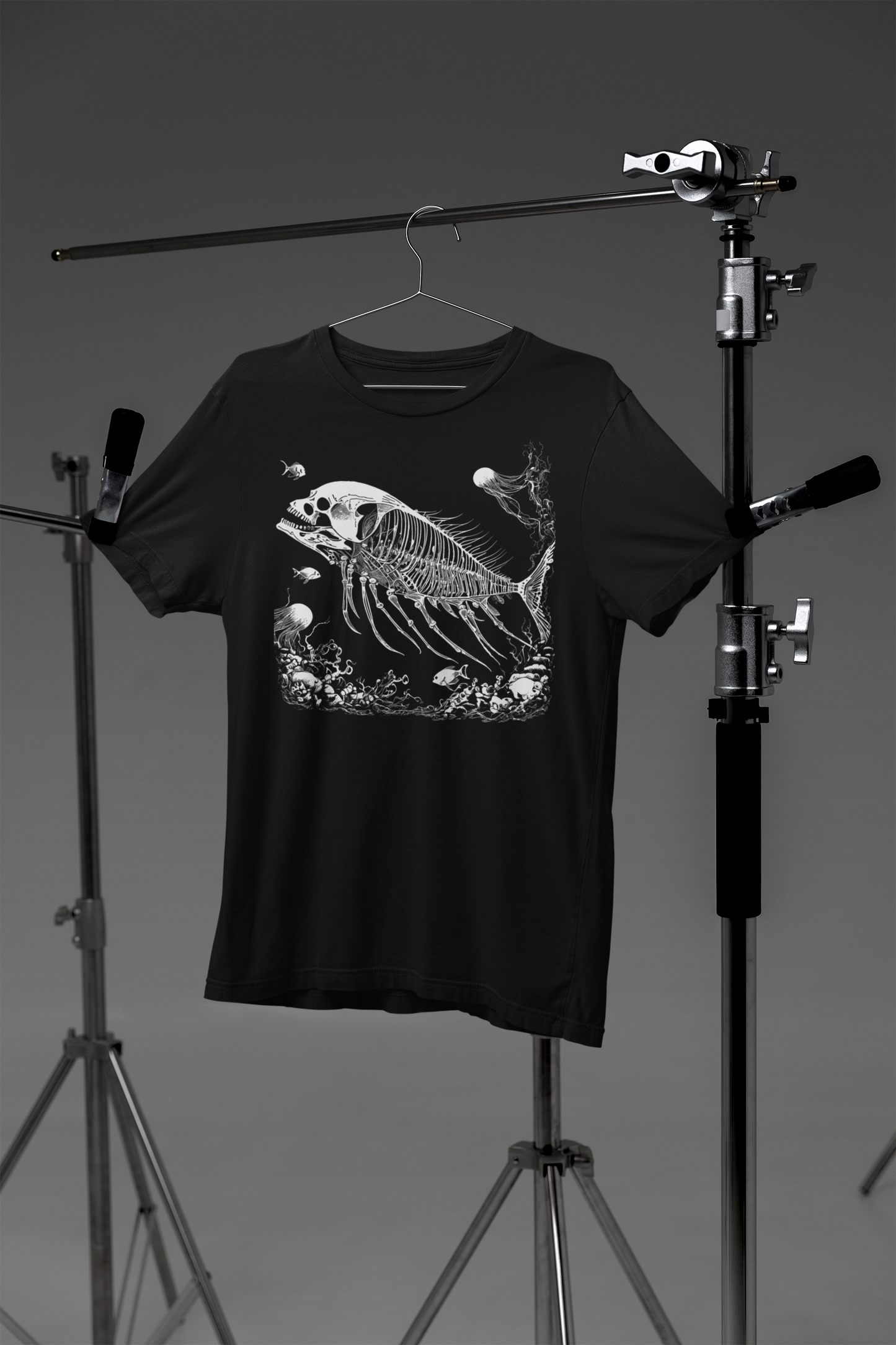 Surreal skeleton fish graphic t-shirt, fossil-inspired fish with skull design, unisex gothic black tee for alternative fashion on a hanger against a gray background