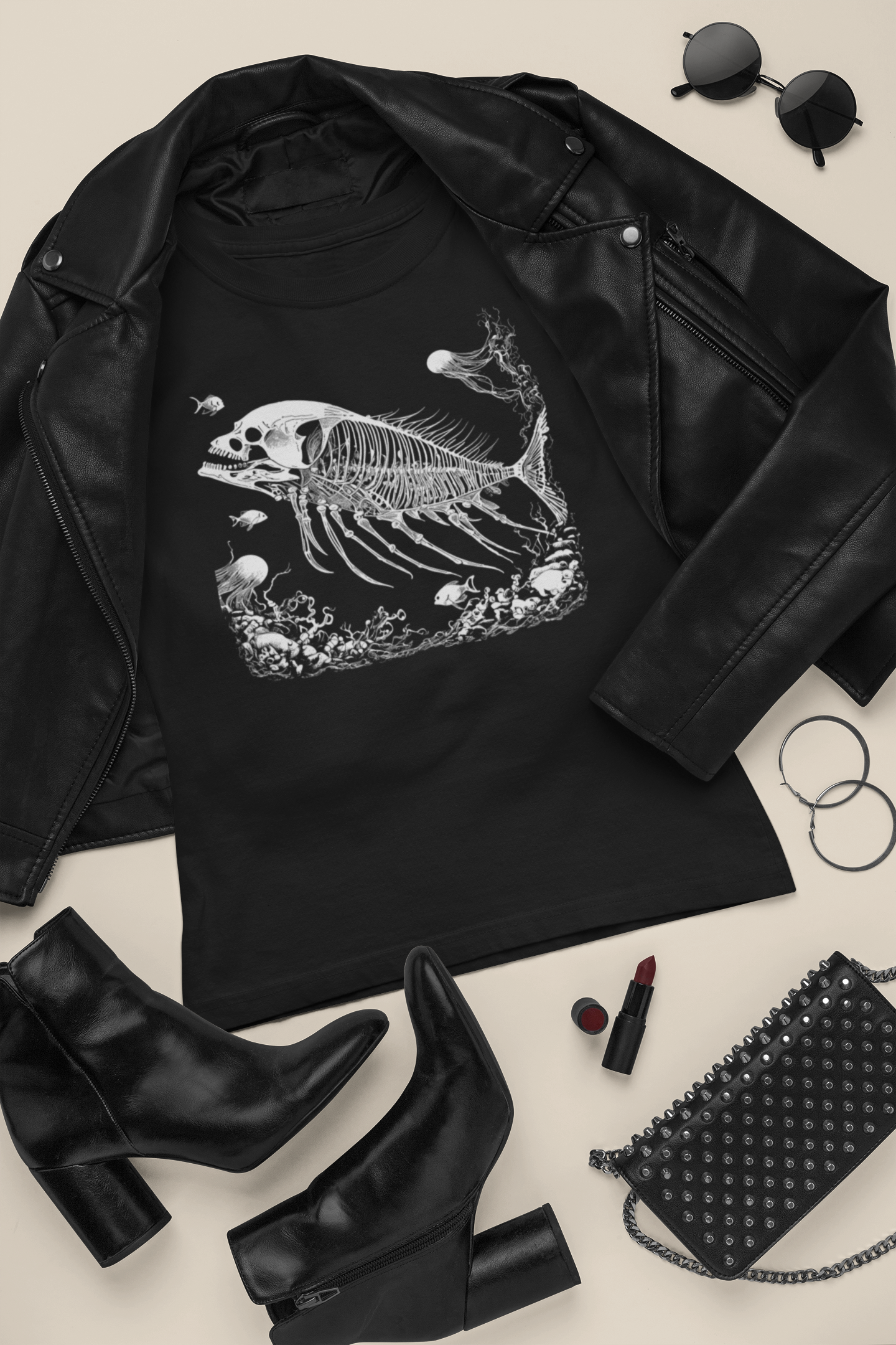 Black t-shirt with surreal skeleton fish design, fossil-inspired artwork with skull and jellyfish, gothic and dark academia fashion, black leather jacket, black boots, and black handbag on a light background